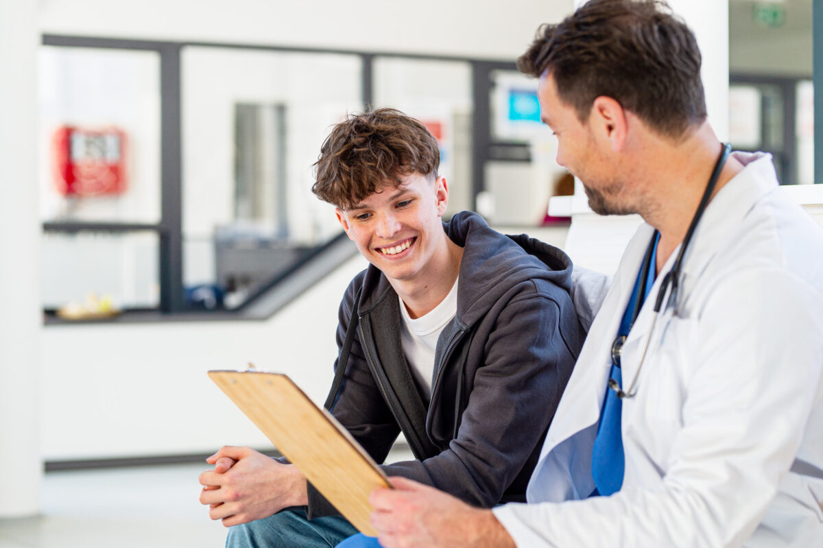 Teenage boy smiling talking with supporting doctor, receiving positive health news.
