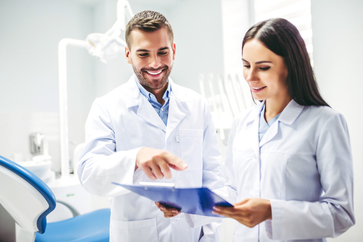 portrait of smiling doctor and assistant looking at clipboard in modern dental clinic