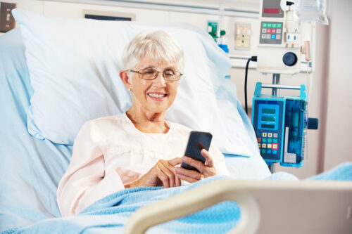 Senior Female Patient In Hospital Bed Using Mobile Phone