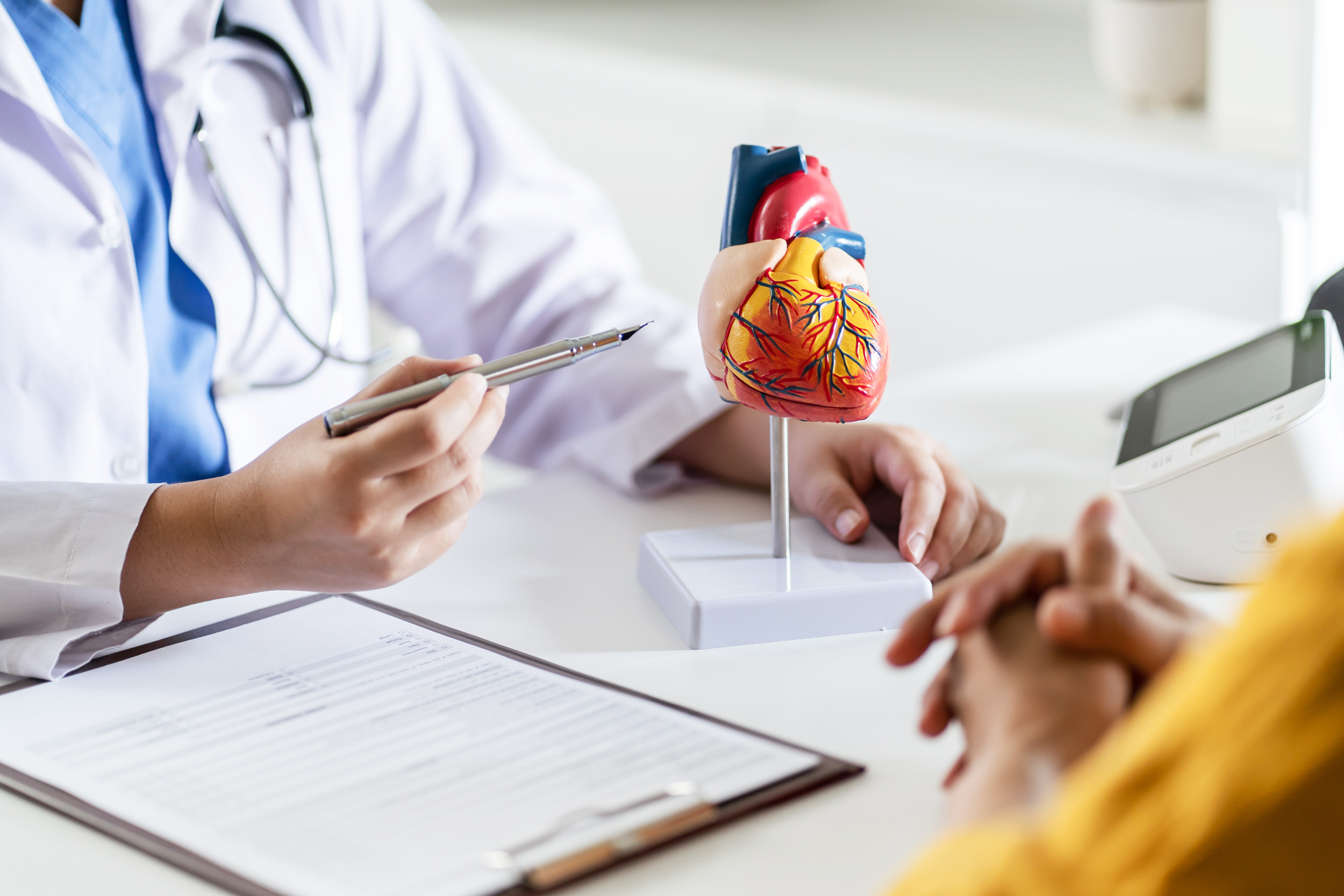 Cardiology Consultation treatment of heart disease. Doctor cardiologist while consultation showing anatomical model of human heart with aged patient talking about heart diseases